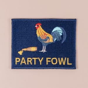 Puede incluir: Parche bordado con fondo azul marino. Presenta una ilustración de gallo colorido y el texto "PARTY FOWL" en amarillo. El gallo tiene detalles rojos, amarillos y azules.