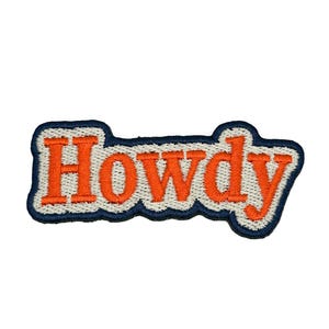 May include: An embroidered patch featuring the word Howdy in bright orange block letters. The text is outlined with a thick white border and finished with a dark navy blue edge, creating a bold, layered appearance with a distinct stitched texture.