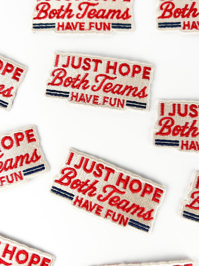 K&ouml;nnte beinhalten: Off-white gestickte Aufn&auml;her mit dem Text "I JUST HOPE Both Teams HAVE FUN" in roter Schrift. Die Aufn&auml;her haben einen marineblauen und roten Rand. Die Aufn&auml;her sind auf wei&szlig;em Hintergrund verstreut.