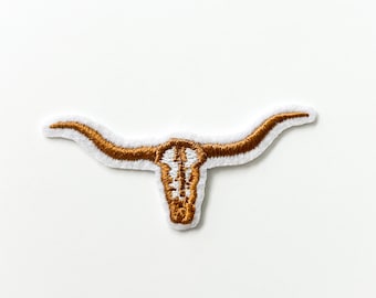 Könnte beinhalten: Ein braunes gesticktes Patch mit einem Longhorn-Schädel mit Hörnern.
