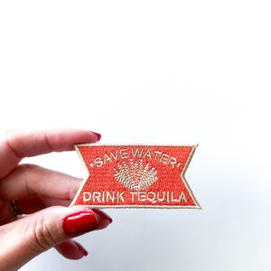 May include: A red embroidered patch with white text that reads "Save Water, Drink Tequila". The patch has a white cactus design in the center.