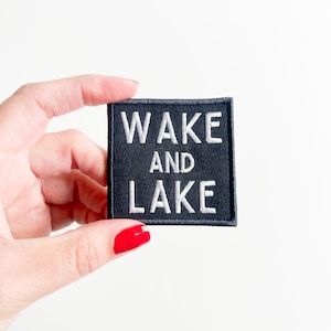 May include: Black fabric patch with white embroidered text that reads "WAKE AND LAKE".