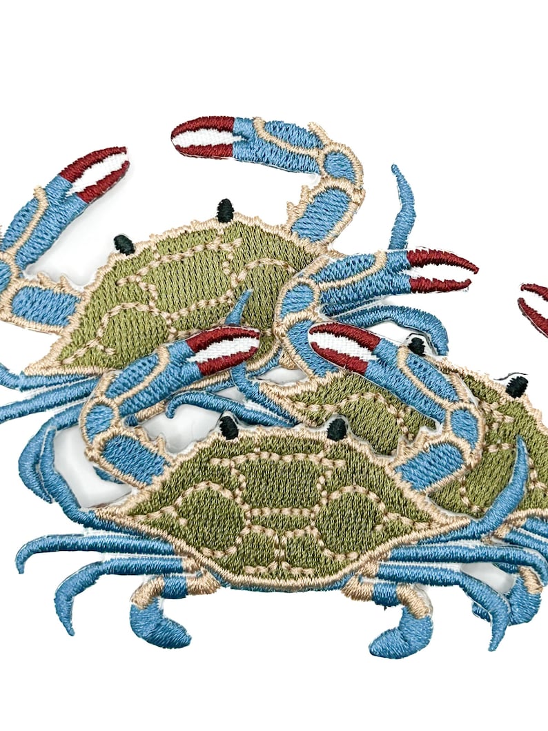 May include: A collection of embroidered crab patches featuring olive green shells with tan outlines and bright blue legs and claws. The claws have distinct red tips and white accents. Each crab has two small black eyes on the top of the shell.