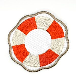 May include: A circular embroidered patch featuring a life preserver design with alternating segments of bright orange and off-white thread. The patch has a white centre and a scalloped, light brown stitched border around the outer edge.
