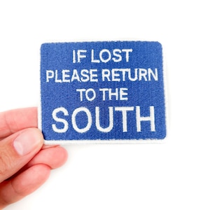 May include: A blue rectangular patch with white embroidered text that reads "IF LOST PLEASE RETURN TO THE SOUTH". The patch is held against a white background.