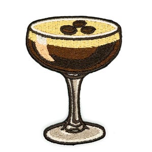 May include: An embroidered patch shaped like a cocktail glass filled with a dark brown liquid, topped with a light tan foam layer and three dark brown coffee beans. The glass features a stem and a circular base with white and brown thread details.