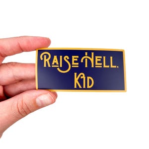 May include: A blue and gold sticker with the text "RAISE HELL. KID" in a stylized font.