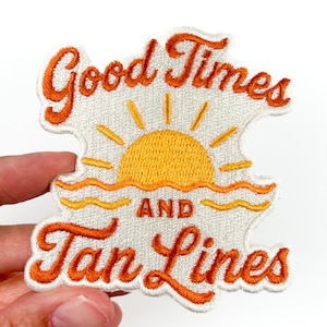Puede incluir: Parche bordado con las palabras "Good Times and Tan Lines" en escritura naranja. El diseño incluye un sol amarillo con rayos y olas naranjas, todo sobre un fondo blanco.