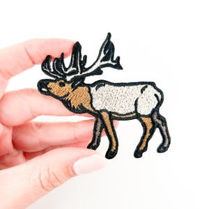 Op de afbeelding: Geborduurde strijkpatch van een bruine en witte eland met zwarte geweien. De eland staat op alle vier poten en kijkt naar links.
