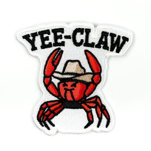 May include: Embroidered patch with a red crab wearing a cowboy hat. The crab has black legs and claws, and the text "YEE-CLAW" is above it in black letters on a white background. The patch has a white border.