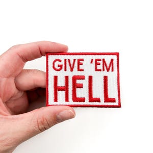 May include: Red embroidered patch with white background. The patch says "Give 'Em Hell" in red lettering.