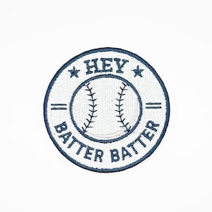 May include: A circular patch with a baseball design and the words "HEY BATTER BATTER" embroidered in navy blue. The baseball graphic is in the center, with the text arranged around it. Two stars flank the word "HEY".