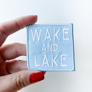 May include: A light blue embroidered patch with white text that reads "WAKE AND LAKE".
