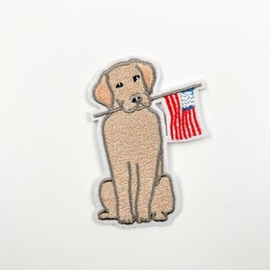 May include: A beige embroidered patch of a dog holding an American flag in its mouth.