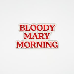 Puede incluir: Un parche rectangular con las palabras "BLOODY MARY MORNING" bordadas en hilo rojo sobre un fondo blanco. El parche tiene un borde blanco y está sobre un fondo blanco liso.
