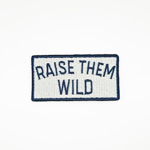 May include: Embroidered patch with the text "RAISE THEM WILD" in dark blue on a white background. The patch has a dark blue border. The patch is rectangular.