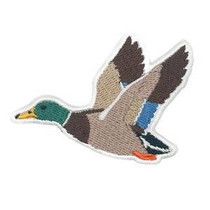 May include: An embroidered patch of a mallard duck in flight, featuring a green head, yellow beak, and wings with brown, tan, and blue feathers. The duck is depicted in profile with its wings spread upward, finished with a white stitched border.