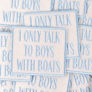 May include: Rectangular patches with light blue embroidered text that reads "I ONLY TALK TO BOYS WITH BOATS." The patches have a light beige background and a light blue border. The patches are scattered.