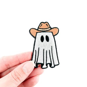 Puede incluir: Un fantasma blanco con un sombrero de vaquero marrón. El fantasma tiene dos ojos negros y un cuerpo blanco parecido a una sábana.