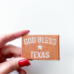 May include: A brown fabric patch with white embroidery that reads "God Bless Texas" with a white star in between the words.