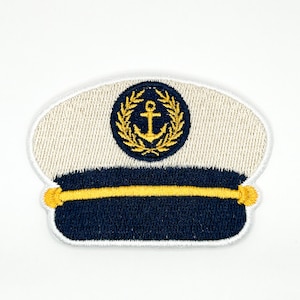 Op de afbeelding: Een geborduurde patch in de vorm van een kapiteinspet. De bovenkant is gebroken wit, de band is donker marineblauw en een gele horizontale lijn loopt door het midden. Een rond embleem toont een geel anker omringd door een gouden lauwerkrans.
