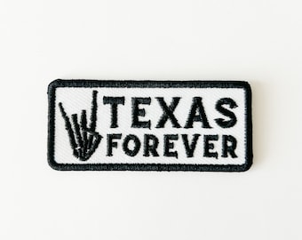 May include: White embroidered patch with black stitching. The patch features a hand gesture with the index and pinky fingers extended and the other fingers closed, along with the text "TEXAS FOREVER".