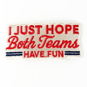 K&ouml;nnte beinhalten: Gestickter Aufn&auml;her mit dem Text "I JUST HOPE Both Teams HAVE FUN" in roter Schrift. Der Aufn&auml;her hat einen beigefarbenen Hintergrund mit zwei blauen Streifen am unteren Rand. Der Aufn&auml;her ist rechteckig.