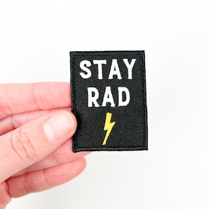 May include: Black iron-on patch with white text that reads "STAY RAD" and a yellow lightning bolt.
