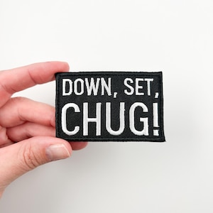 Peut inclure: Patch thermocollant noir avec broderie blanche qui dit "DOWN, SET, CHUG!"