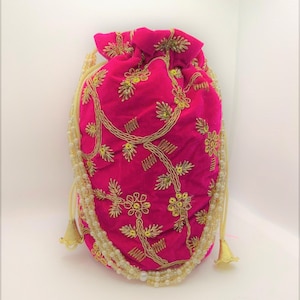 May include: A pink velvet drawstring bag with gold embroidery and a white pearl trim. The bag has a tassel on each side.