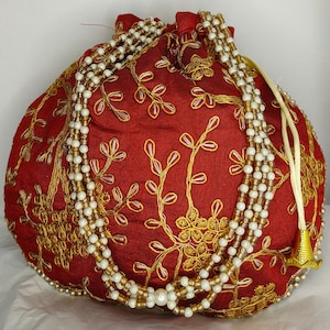 May include: A red drawstring bag with gold embroidery of floral designs. The bag is adorned with a white and gold beaded necklace.