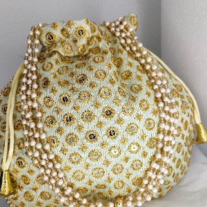 May include: A white drawstring bag with gold embroidery and a pearl trim. The bag is decorated with a repeating pattern of small circles.