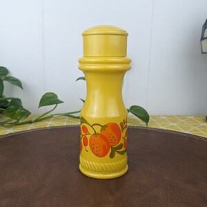 May include: Yellow ceramic bottle with a painted design of orange fruit and green leaves. The bottle has a cork top.