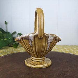 以下が含まれることがあります： 白く釉薬がかけられた茶色の陶器製のバスケットで、フルーティングのデザインとハンドルが付いています。バスケットは茶色の表面の上に置かれています。