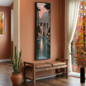 May include: A tall, rectangular framed wall art piece depicting a classical architectural structure with columns and a dome, reflected in a calm body of water under a soft pink sky. The artwork features lush greenery and warm lighting accents.