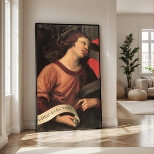 May include: A framed vertical wall art print featuring a classical painting of a person with wavy brown hair and a thin halo, wearing a reddish-brown tunic. The figure holds a white scroll with the text A DEO ELECTVS in black lettering.