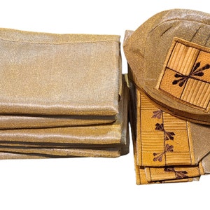 May include: A stack of gold-colored fabric napkins and matching placemats. The placemats have a square embroidered design with a floral motif. The napkins and placemats are made of a shimmering, textured material.