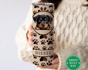 May include: A stainless steel tumbler featuring a Rottweiler puppy illustration. The tumbler has a tan background with paw prints and a circular design with the puppy's face. The name "DIESEL" is printed on the tumbler.