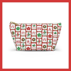 May include: White zippered pouch featuring a repeating pattern of red, green, and white Mahjong tiles. The tiles display Chinese characters, flowers, and dragons. The pouch has a gold zip.