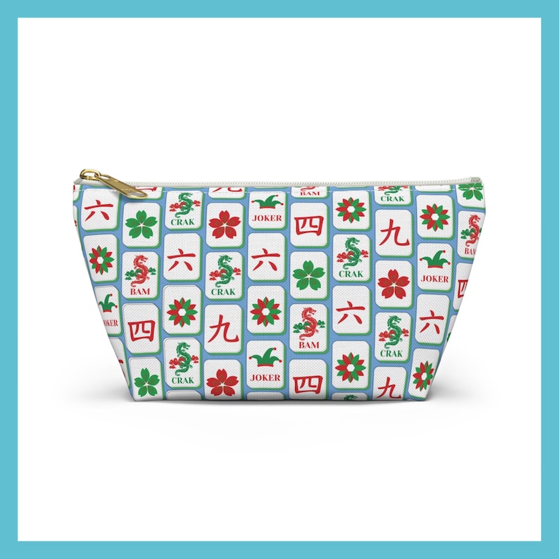 May include: A rectangular cosmetic bag with a gold zipper. The bag is patterned with white tiles featuring red, green, and black symbols and characters. The bag's design includes the words "Crak", "Bam", and "Joker".
