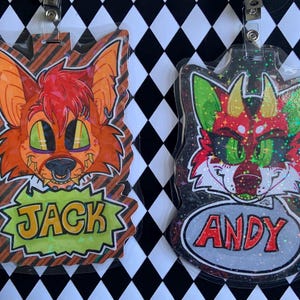 May include: Two cartoon badges featuring anthropomorphic fox-like characters. One is orange with the name "JACK" in a green bubble, the other is red and green with the name "ANDY" in a gray bubble. Both are in plastic holders.