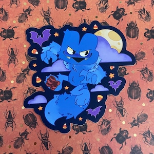 May include: A blue monster with a toothy grin, wearing a purple scarf, is leaping through the air. The monster is surrounded by stars, bats, and candy corn. A full moon shines in the background.