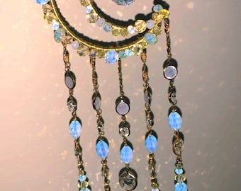 May include: A gold wire crescent moon with crystal beads and a crystal prism hanging from the bottom. The moon is decorated with clear and iridescent beads.
