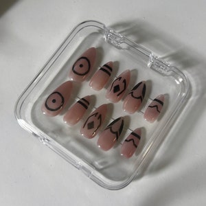 May include: A clear plastic case with ten nude-colored false nails. Each nail has a different black geometric design.
