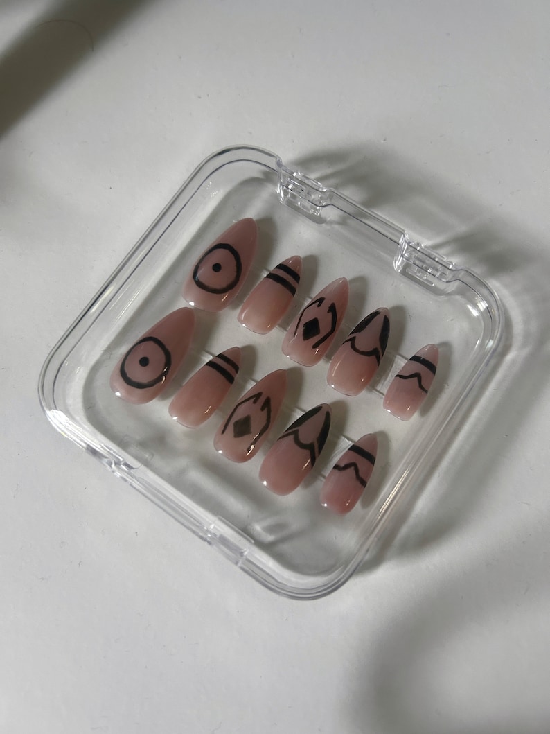 May include: A clear plastic case with ten nude-colored false nails. Each nail has a different black geometric design.