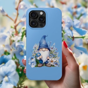 May include: A blue phone case with a white gnome holding a blue flower surrounded by blue and white flowers. The phone case has a camera lens on the back.