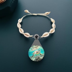 May include: A white seashell bracelet with a round pendant featuring a sea turtle swimming in blue water.
