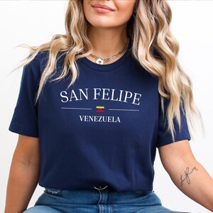 May include: Navy blue t-shirt with the text "SAN FELIPE" in white, with a horizontal line and the word "VENEZUELA" below. A small Venezuelan flag is above the word "VENEZUELA".