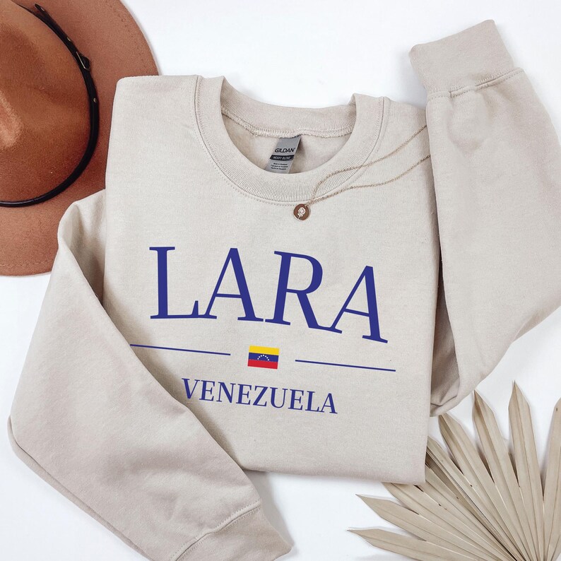 Pu&ograve; includere: Una felpa beige con il testo "LARA VENEZUELA" in blu e un piccolo grafico della bandiera venezuelana.