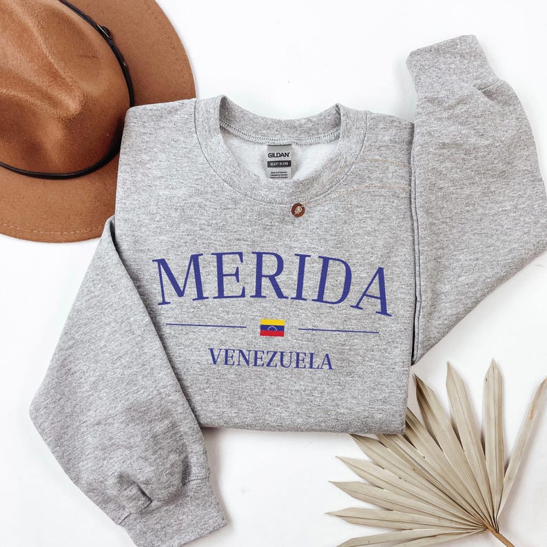 Pu&ograve; includere: Felpa grigia con il testo "MERIDA VENEZUELA" in lettere blu. Una piccola bandiera venezuelana &egrave; stampata tra le parole.